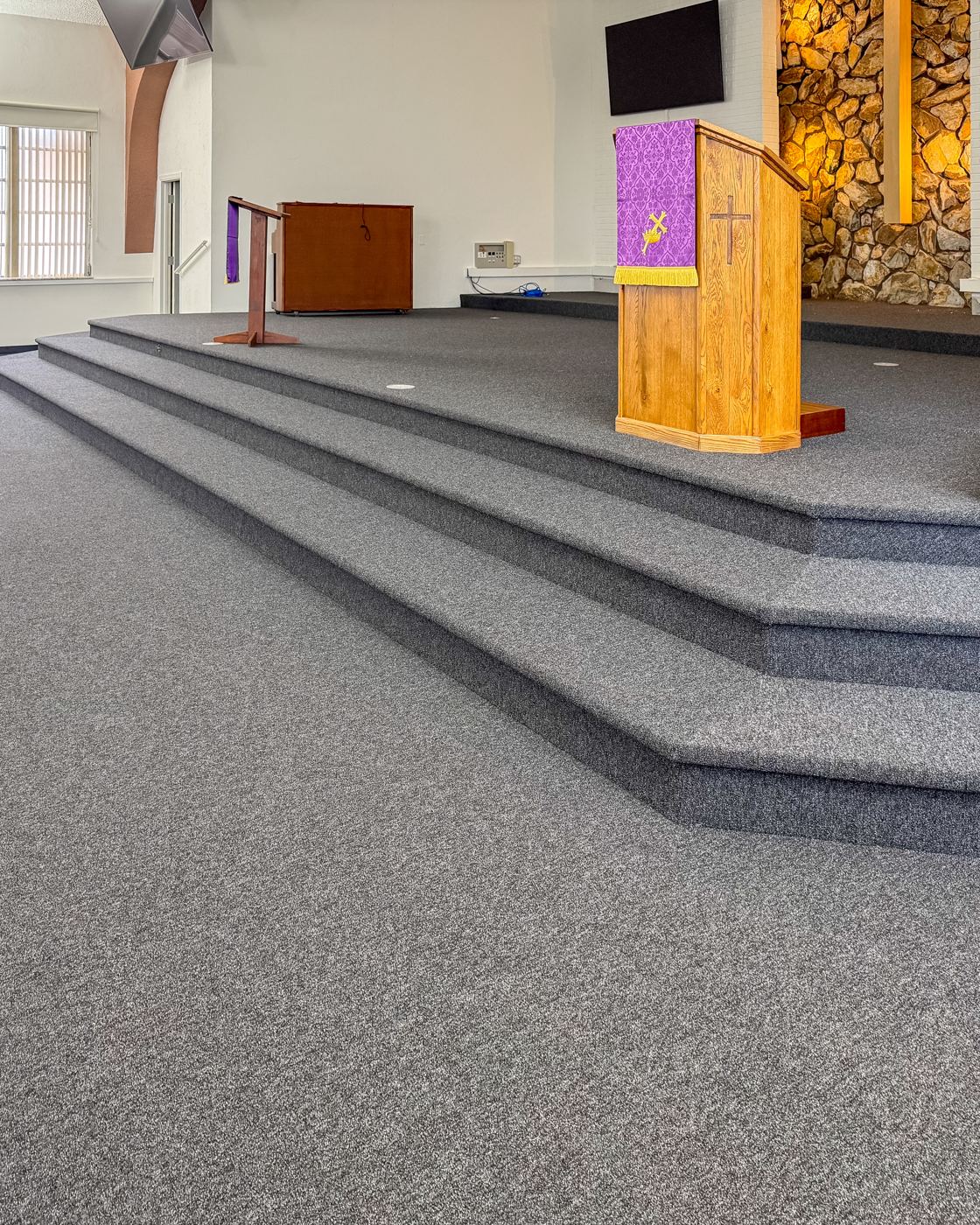 New carpet wrapped cleanly over the altar steps beside the wooden pulpit with its purple parament.