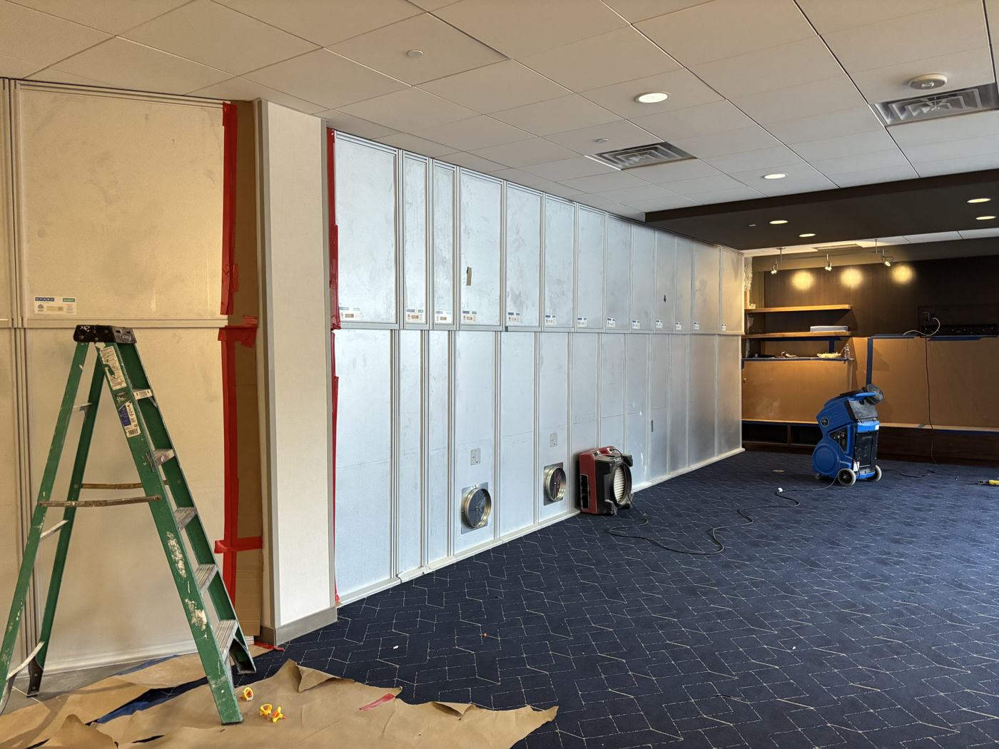 The work side of the same wall: negative-air machines ducted through sealed panels, kraft paper on the floor, renovation underway.