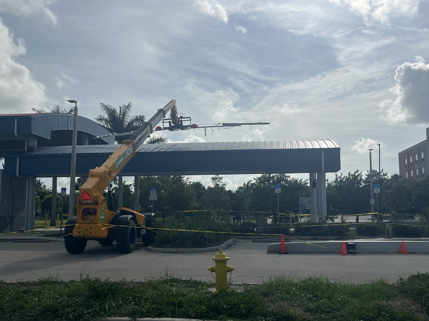 Telehandler lifting a canopy panel behind caution tape while the park-and-ride stays open behind it.
