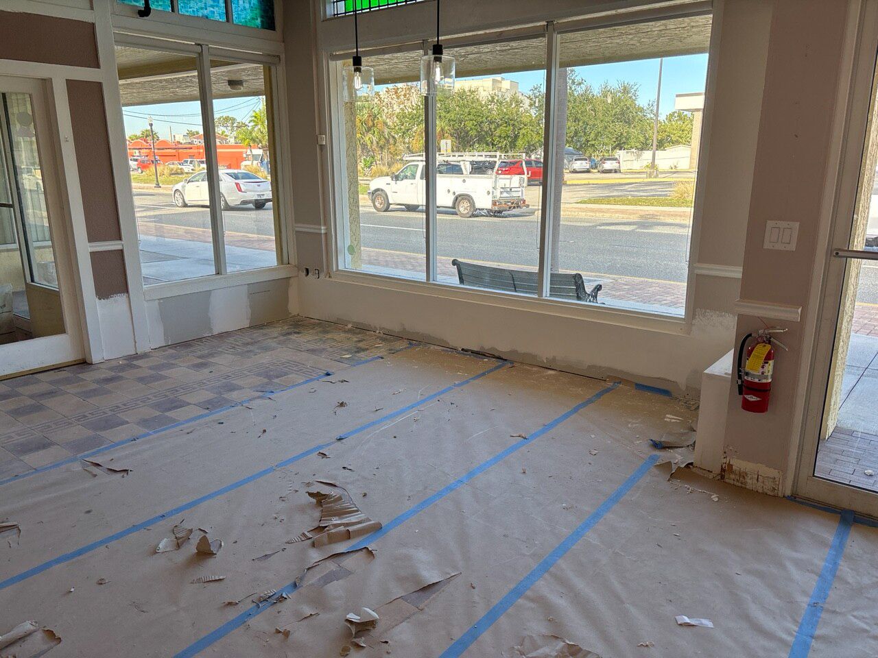 Salon storefront mid-rebuild: floors under protective paper and tape, walls patched, street visible through the front glass.